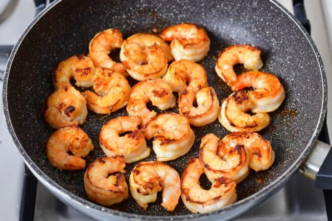 Shrimp is being seared in a black skillet.