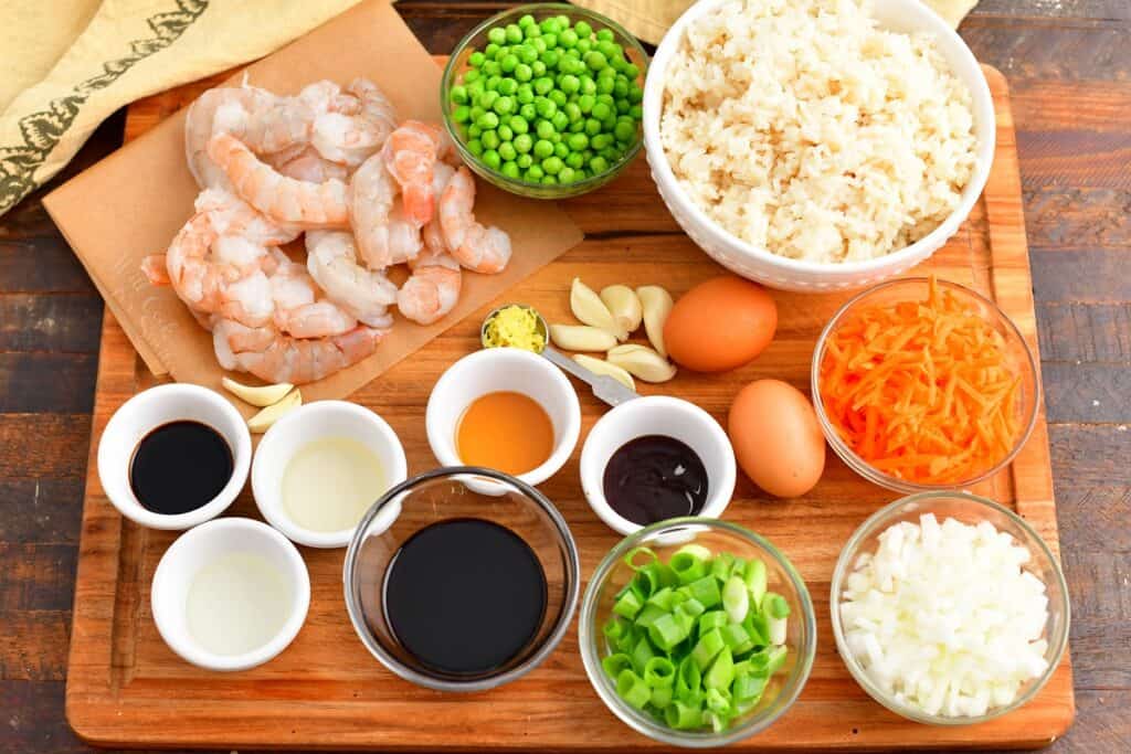 The ingredients for shrimp fried rice are on a wooden cutting board. 