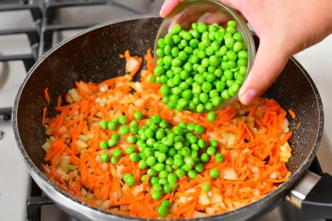 Peas are being poured on top of carrots and onions in a warm pan.