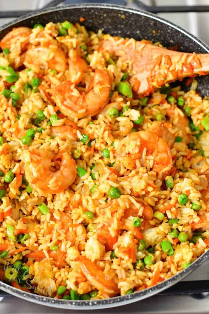 A wooden spoon is placed in a pan filled with shrimp fried rice.