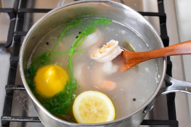 Shrimp, lemon and herbs are being cooked in a large pot filled with water. 