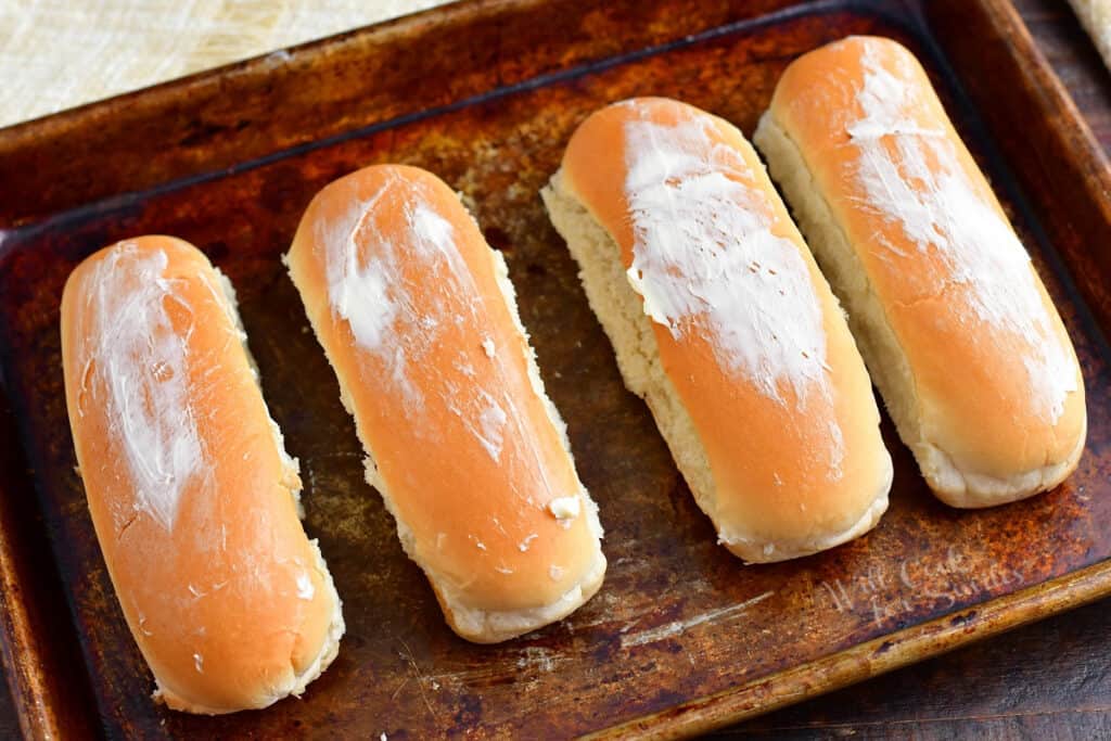 Butter is smeared on four different hot dog buns.
