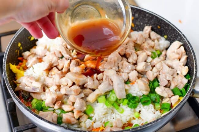 pouring brown sauce into the pan with rice, chicken, and vegetables