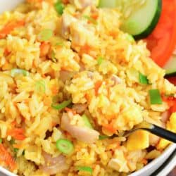 close up and scooping Thai fried rice in a bowl with cucumber and tomato slices