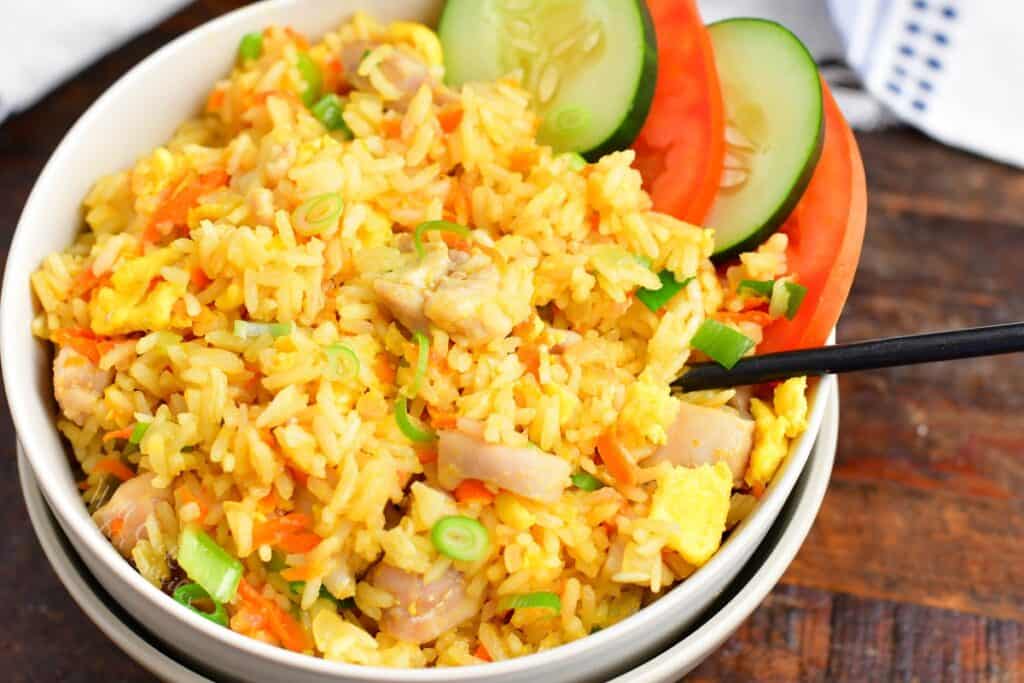 side view of Thai fried rice in a bowl with cucumber and tomato slices