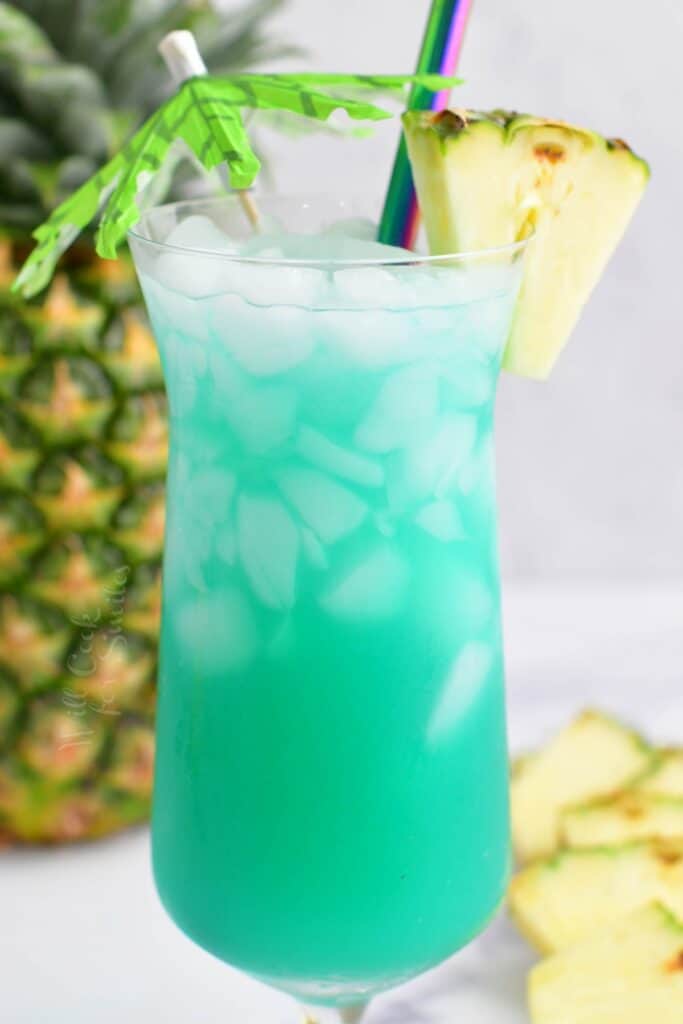 closeup side view of blue cocktail in a glass with pineapple and umbrella
