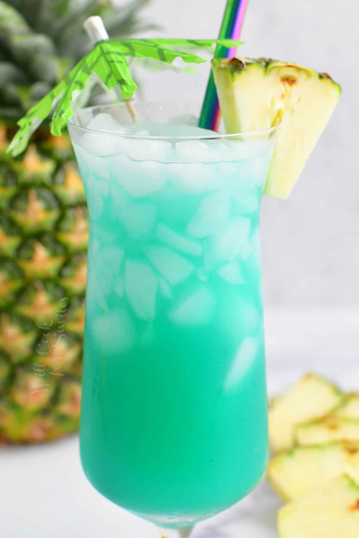 closeup side view of blue cocktail in a glass with pineapple and umbrella