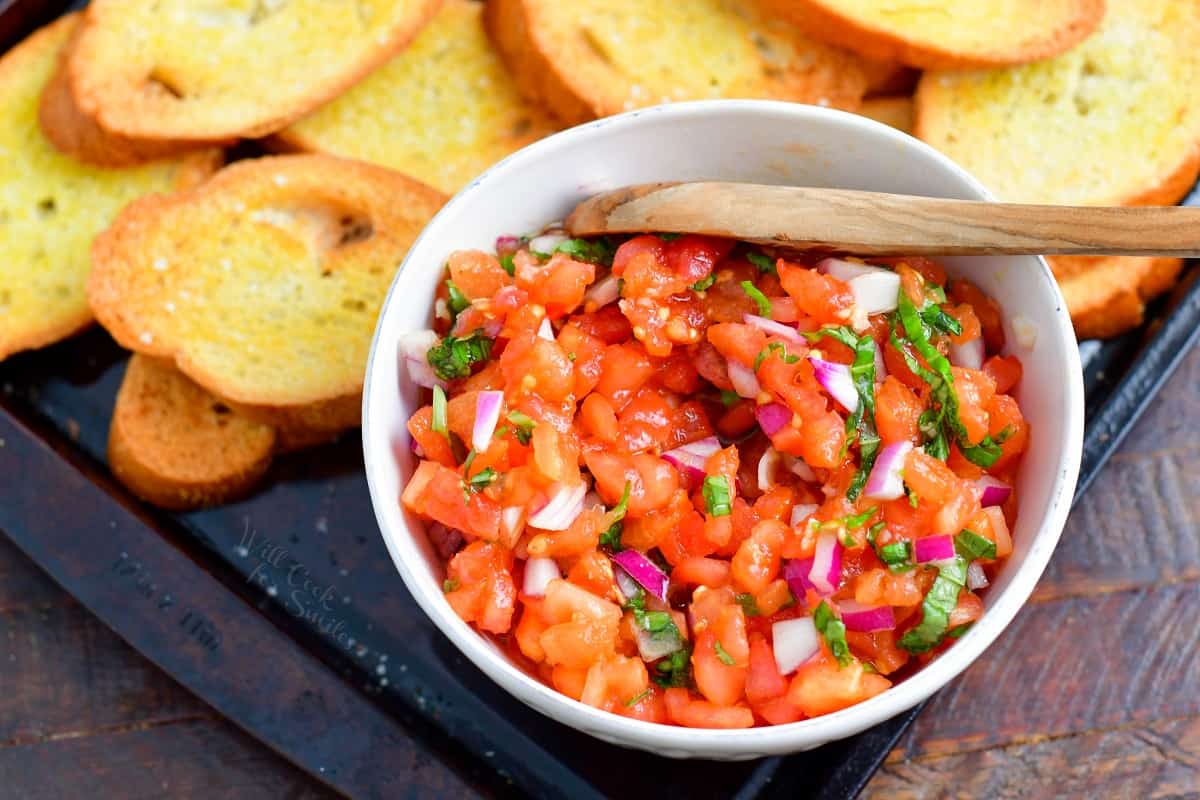 diced tomato mixture for bruschetta in a white bowl with toasted bread next to it