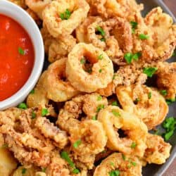 Calamari is plated with a small bowl of red dipping sauce.