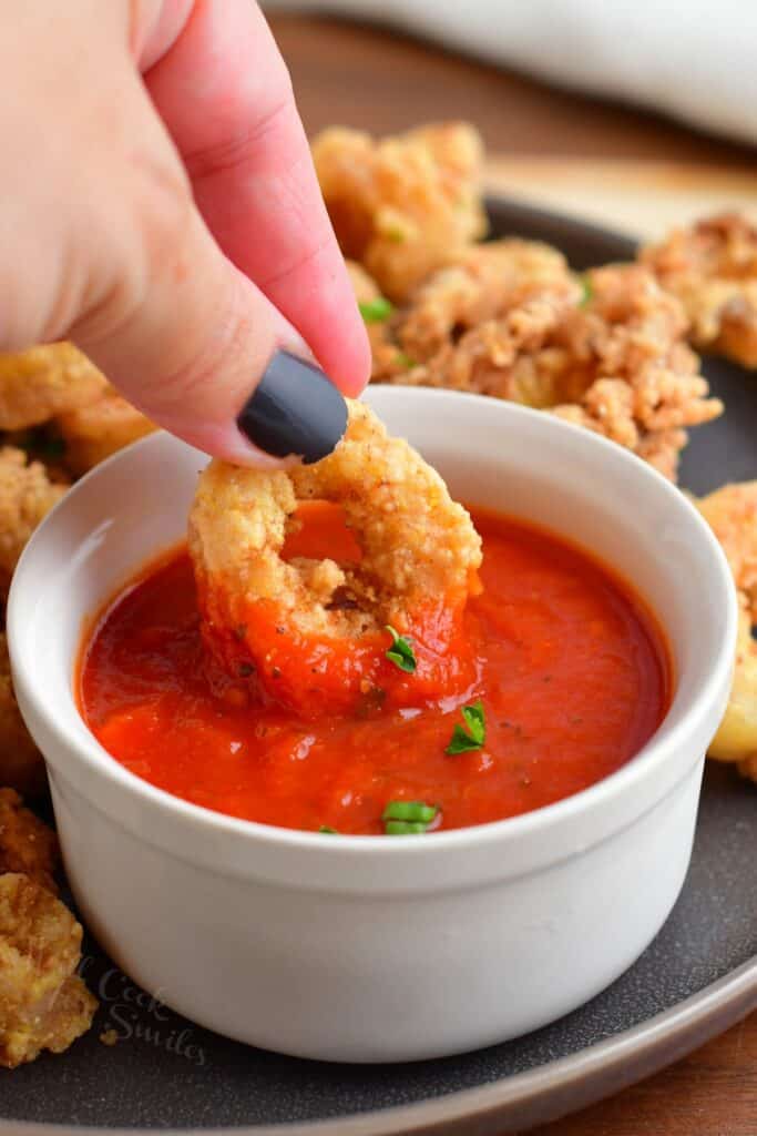 A calamari ring is being dipped into marinara sauce. 