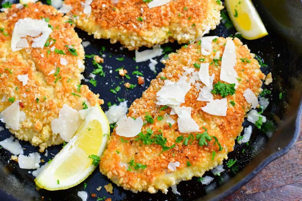 Lemon wedges, parmesan and parsley are in a pan with cooked chicken. 