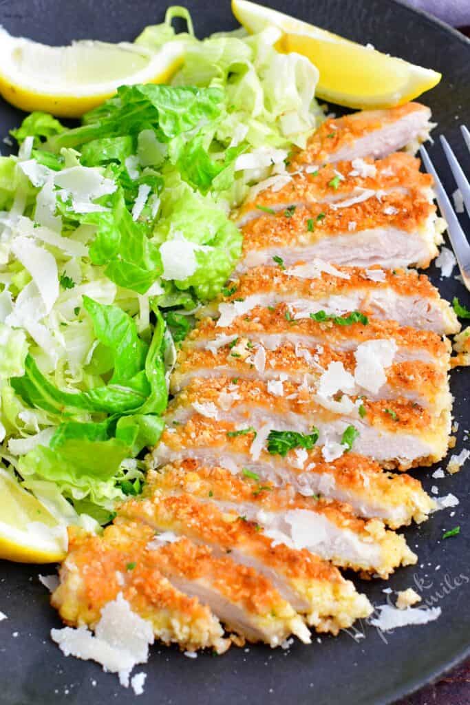 Sliced chicken milanese is placed next to a fresh green side salad. 