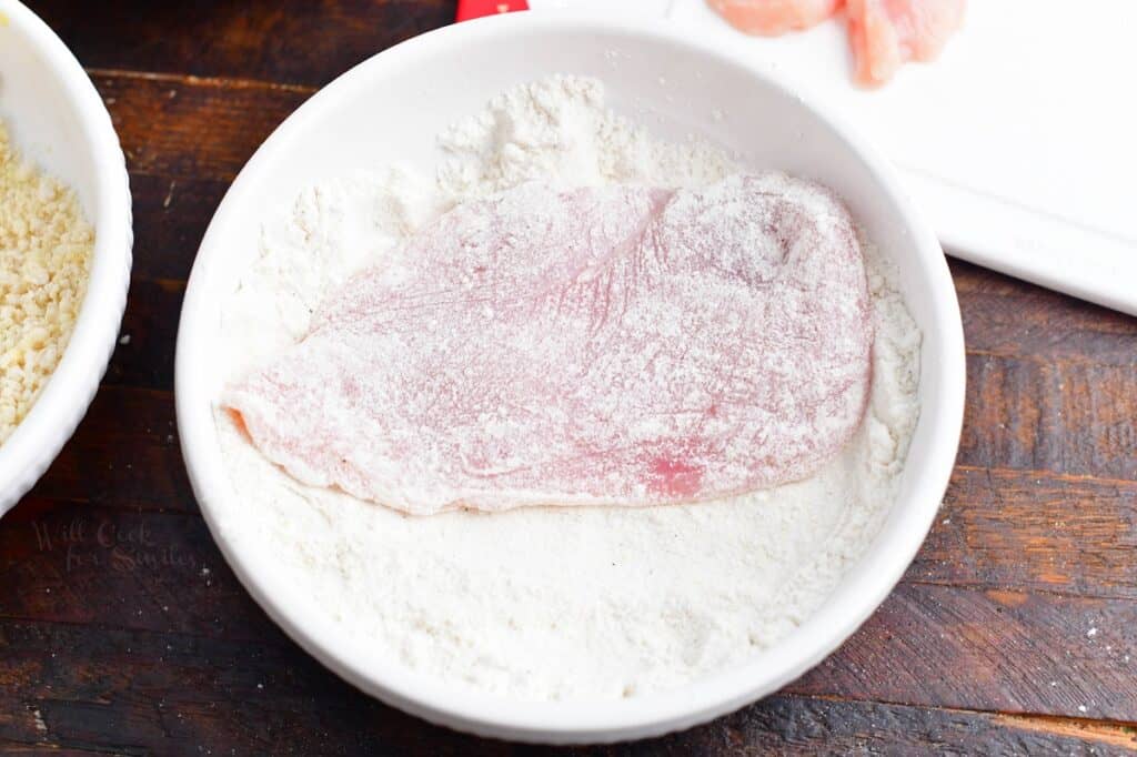 Chicken is being dipped into a bowl filled with powder.