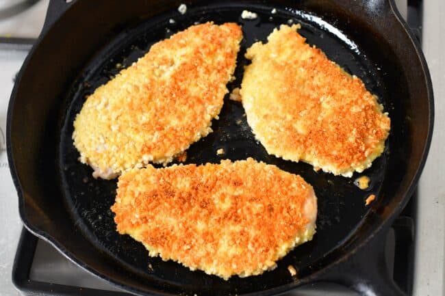 Golden brown chicken is in a black pan.