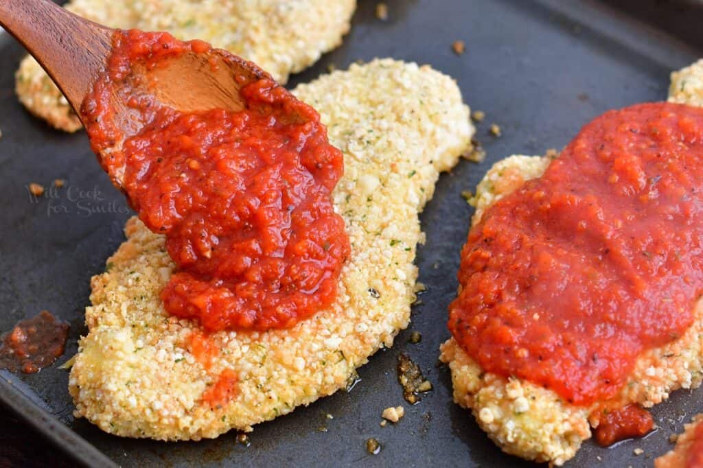adding easy marinara sauce over crispy baked chicken
