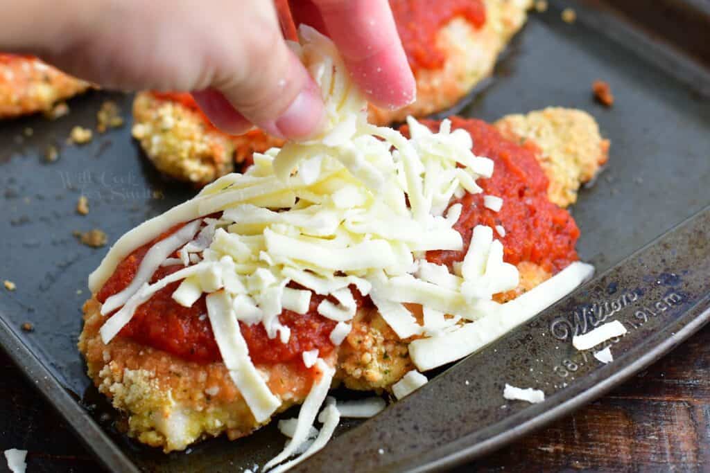 adding shredded mozzarella cheese on top of sauce on baked chicken