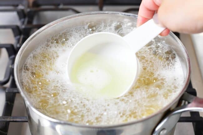 scooping cooking water out of a bowl of pasta boiling in a pot