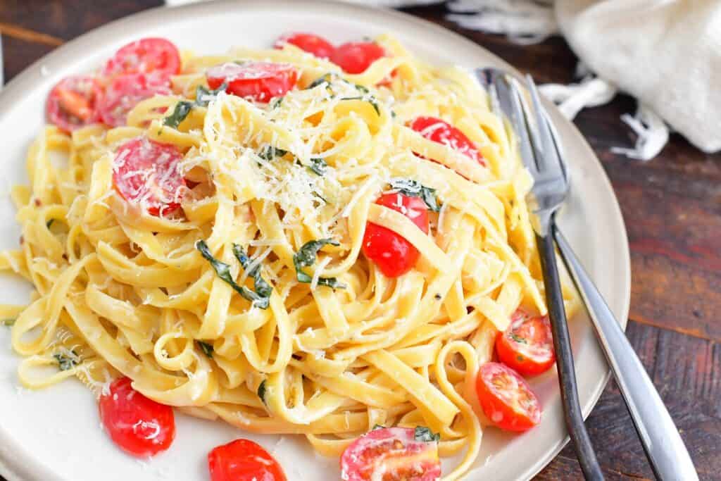 fettuccine in cream sauce with tomatoes and basil on a place with fork and spoon