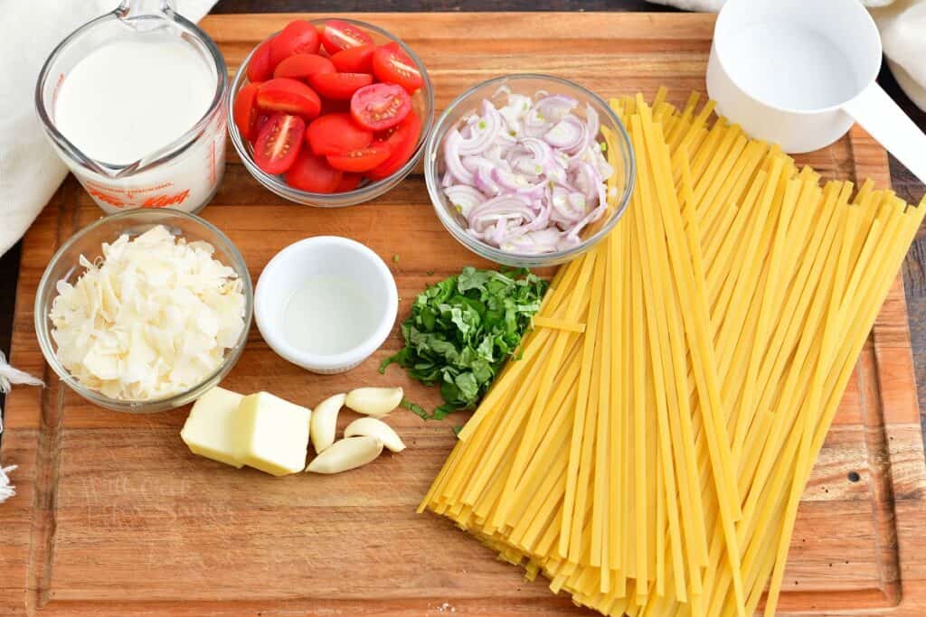 ingredients to creamy fettuccine with tomatoes and basil on a cutting board