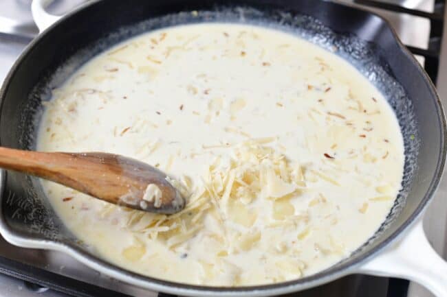 stirring in shaved Parmesan into the cream sauce in a pan