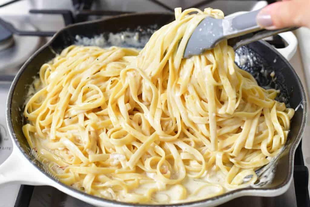 tossing fettuccine in cream sauce in a pan