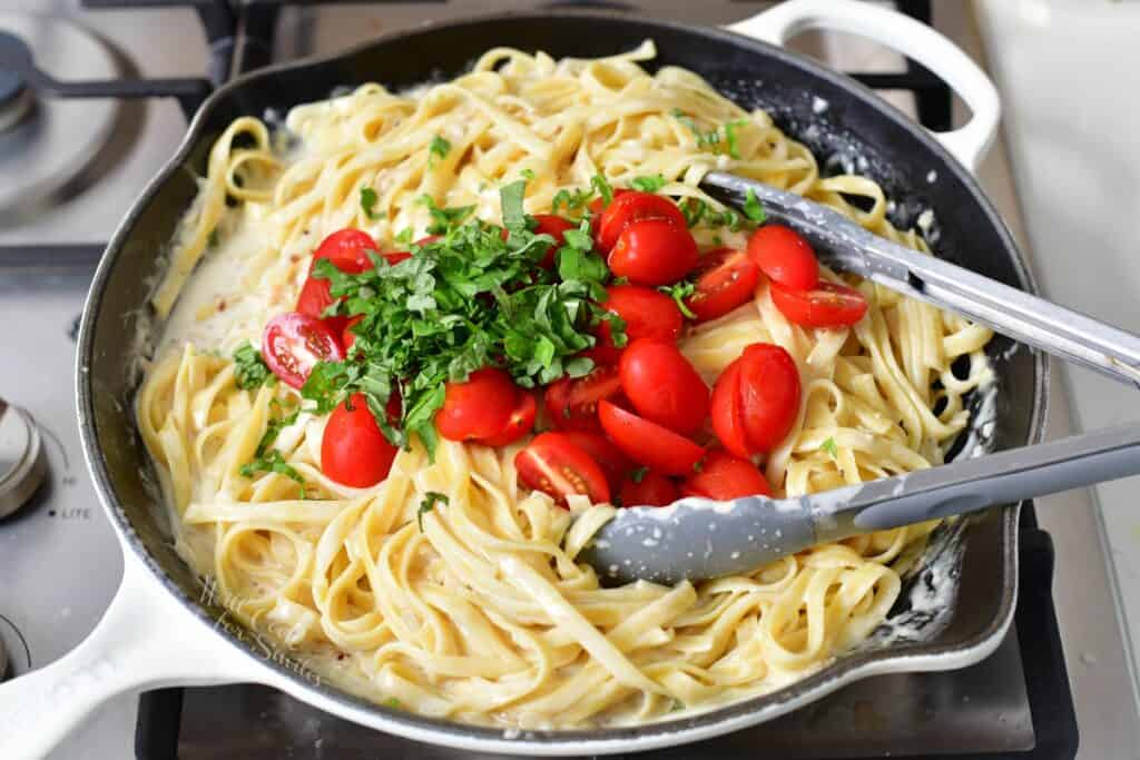 added tomatoes and basil to the pasta in cream sauce in a pan