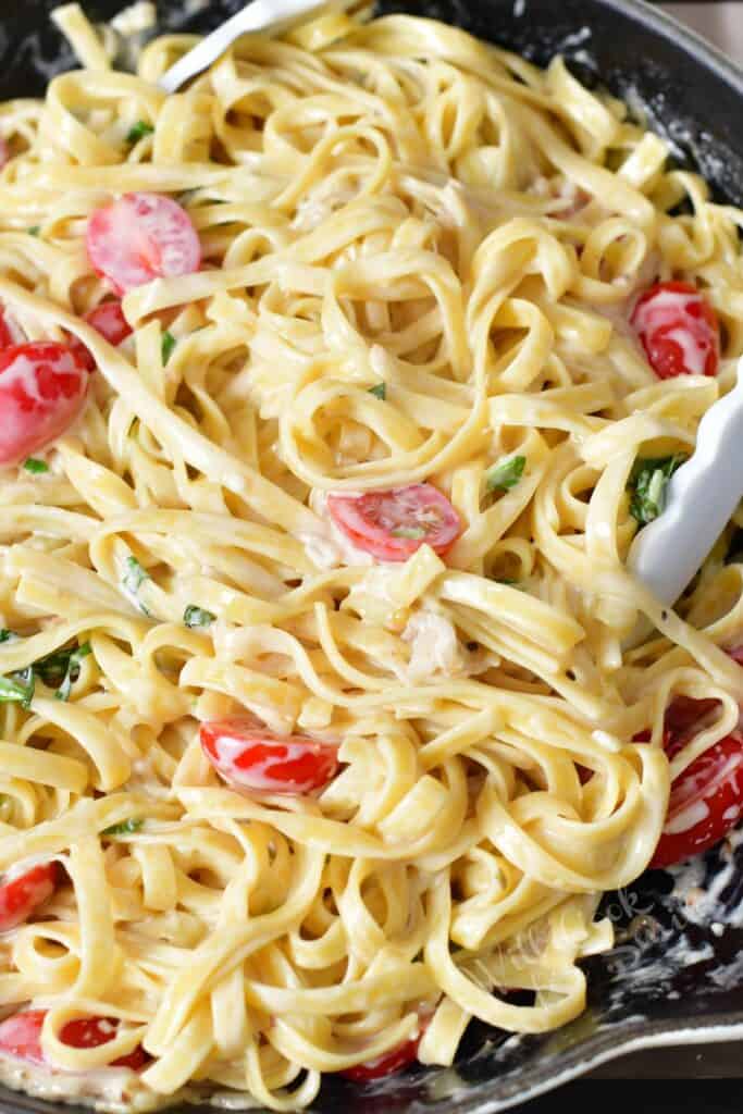 closeup of pasta tossed in cream sauce with tomatoes in a cooking pan