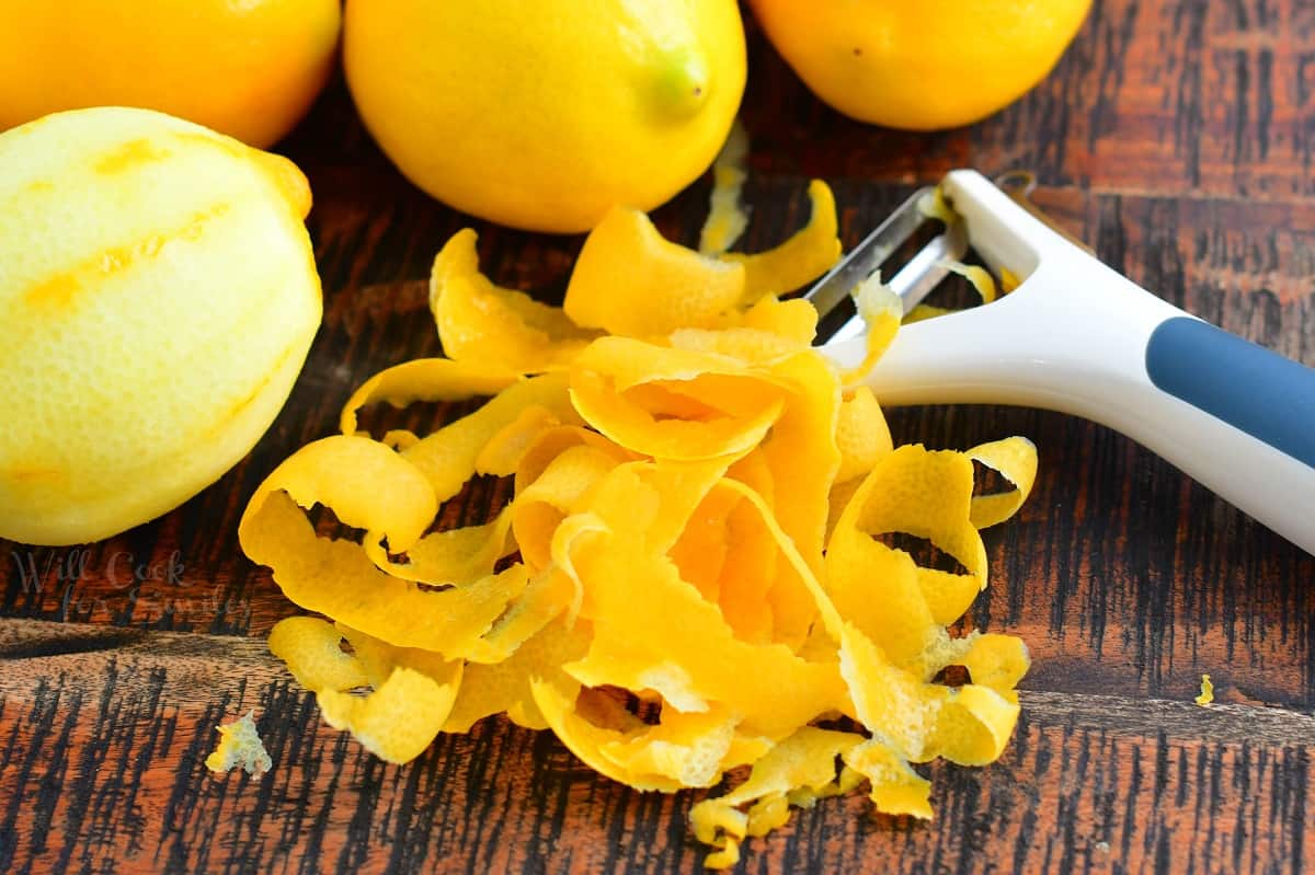 A vegetable peeler has removed lemon skins on a wooden surface.