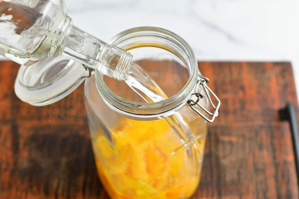 Vodka is being poured into a glass jaw with lemon peels.