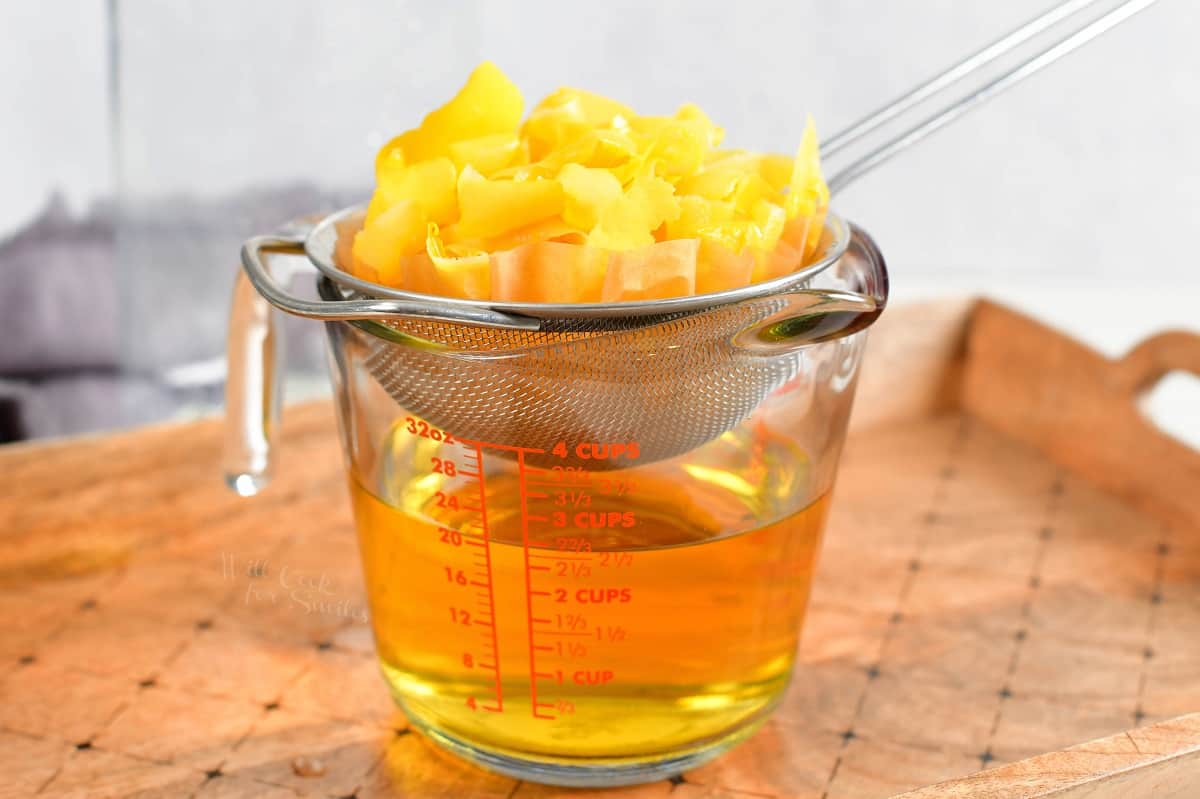 Lemon peels are placed on a mesh strainer above a measuring cup now filled with lemon vodka.