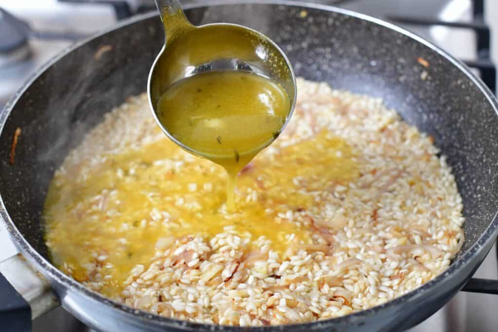 adding broth to the rice cooking in the pan