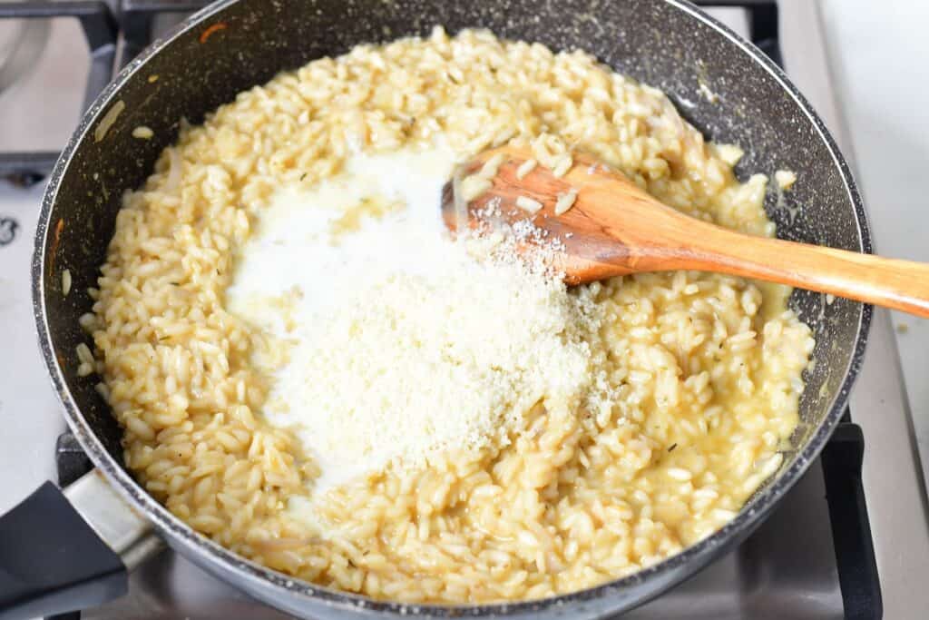adding cream and parmesan cheese to the rice in the pan