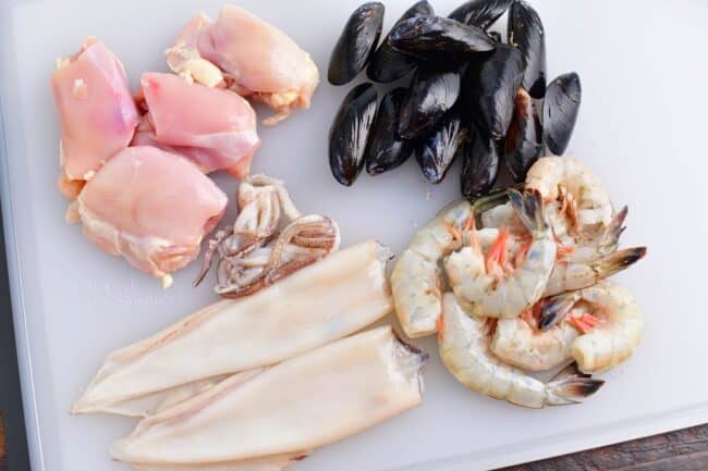 Different meats are placed on a white cutting board. 