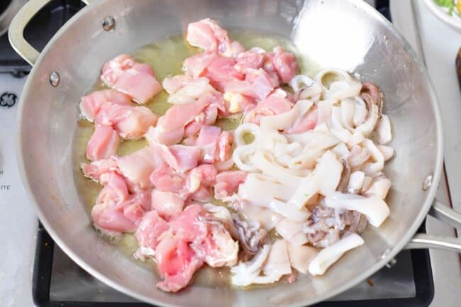 Chicken and calamari are being seared in a pan.