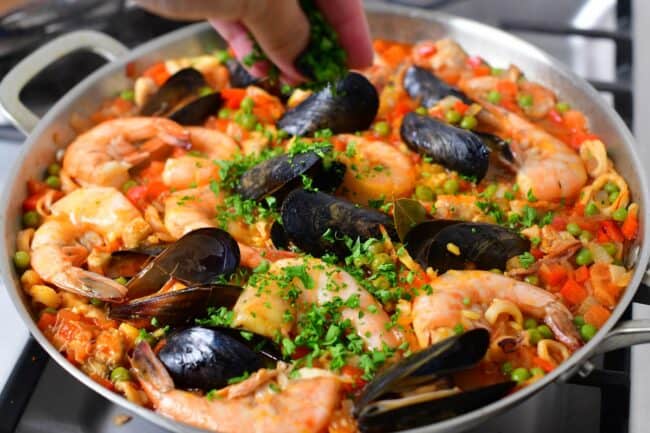 Parsley is being sprinkled on top of cooked paella.