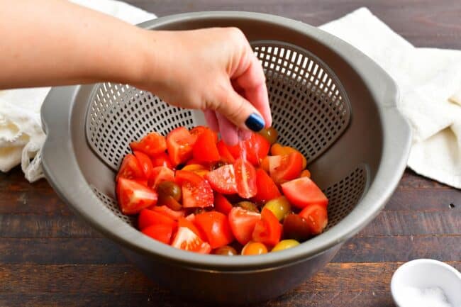 adding salt to cut tomatoes in a colander 