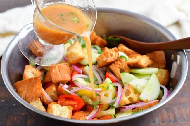 adding tomato vinaigrette to the bowl with vegetables and bread