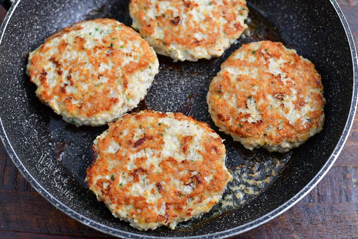 four cooked chicken burger patties in a large pan.