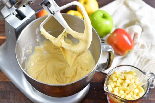 The batter is being mixed in a bowl, while a cup of diced apples sits on the side.