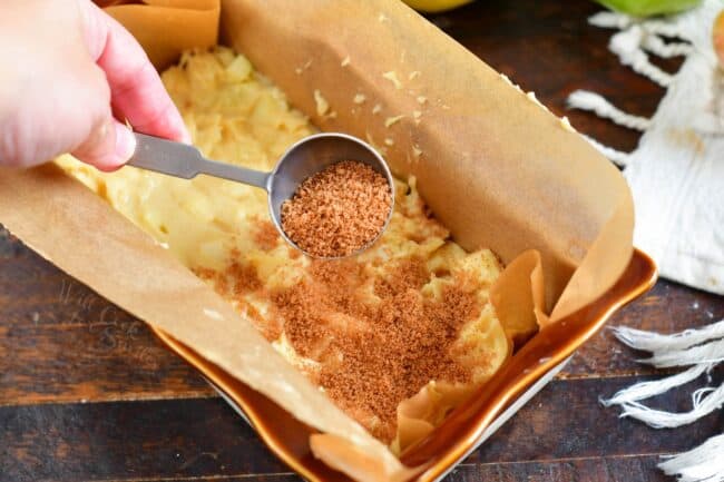 Cinnamon sugar is being sprinkled on top of the bread batter in a prepared baking dish.