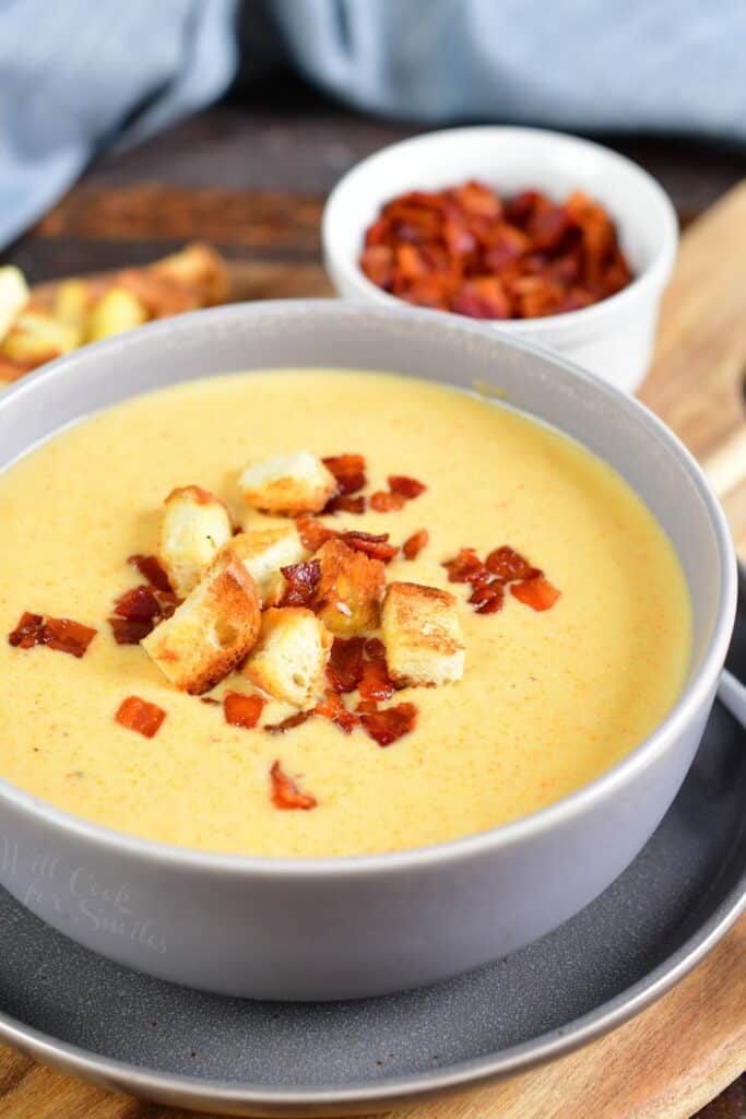 cheddar ale soup in grey bowl with bacon bits and croutons