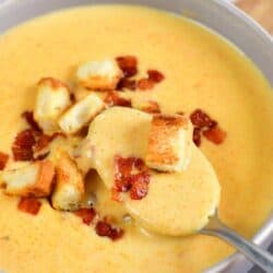 spooning some cheddar ale soup out of the bowl with croutons and bacon on top