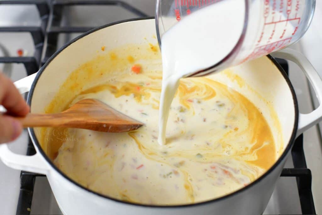 adding milk to the soup in a white pot