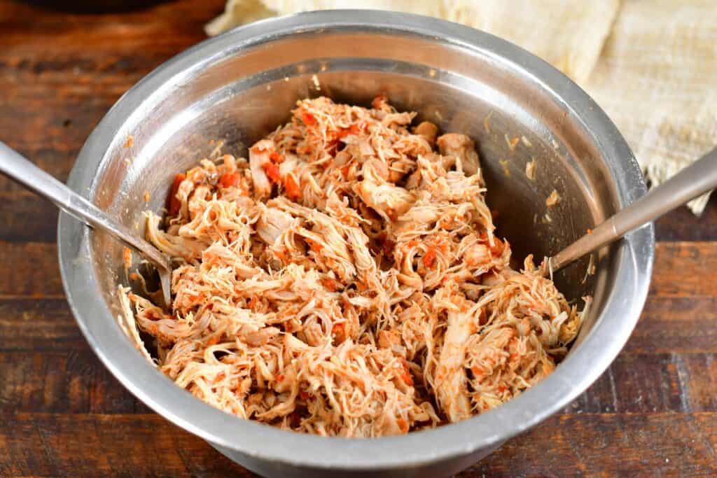 shredding cooked chicken in a metal bowl with two forks