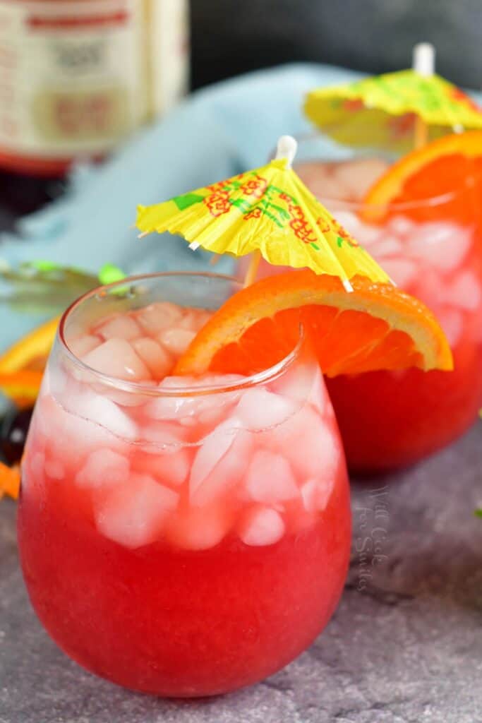 Two glasses are filled with a summery sweet cocktail on a gray countertop. 