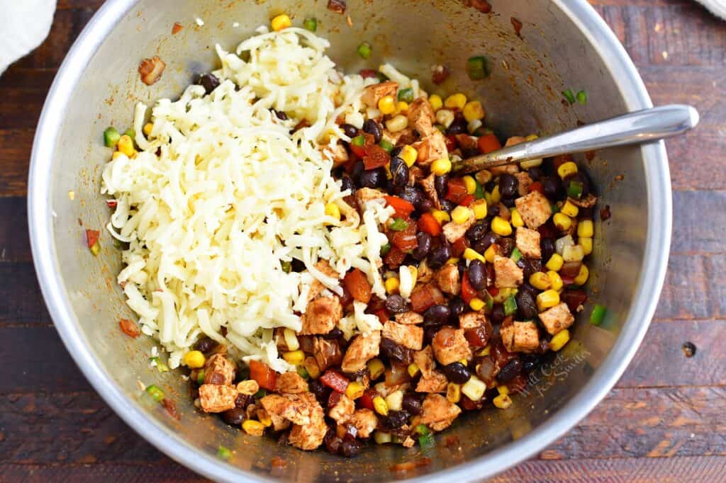 adding cheese to the chicken filling in a metal bowl