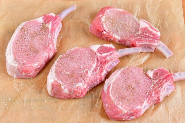 Raw pork chops are resting on a sheet of parchment paper.