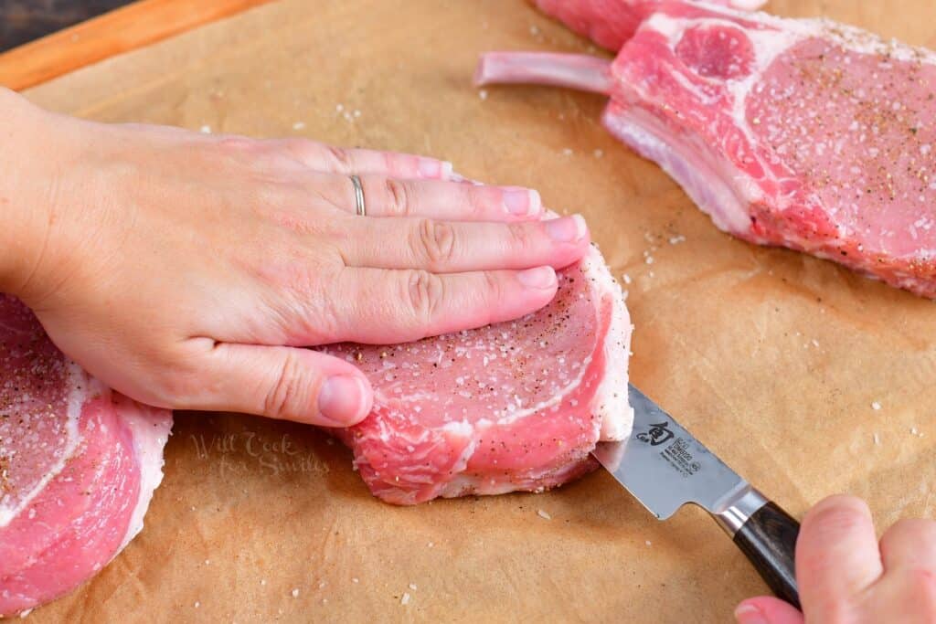 Raw pork chops are being sliced in half.