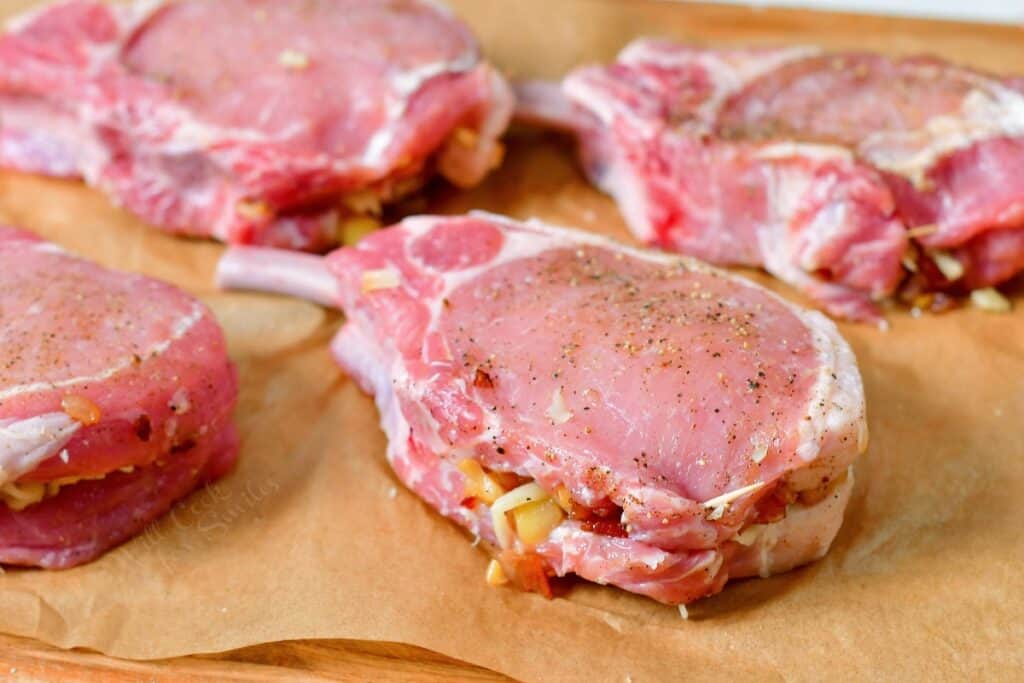 Raw pork chops are stuffed and placed on a prepared baking sheet.