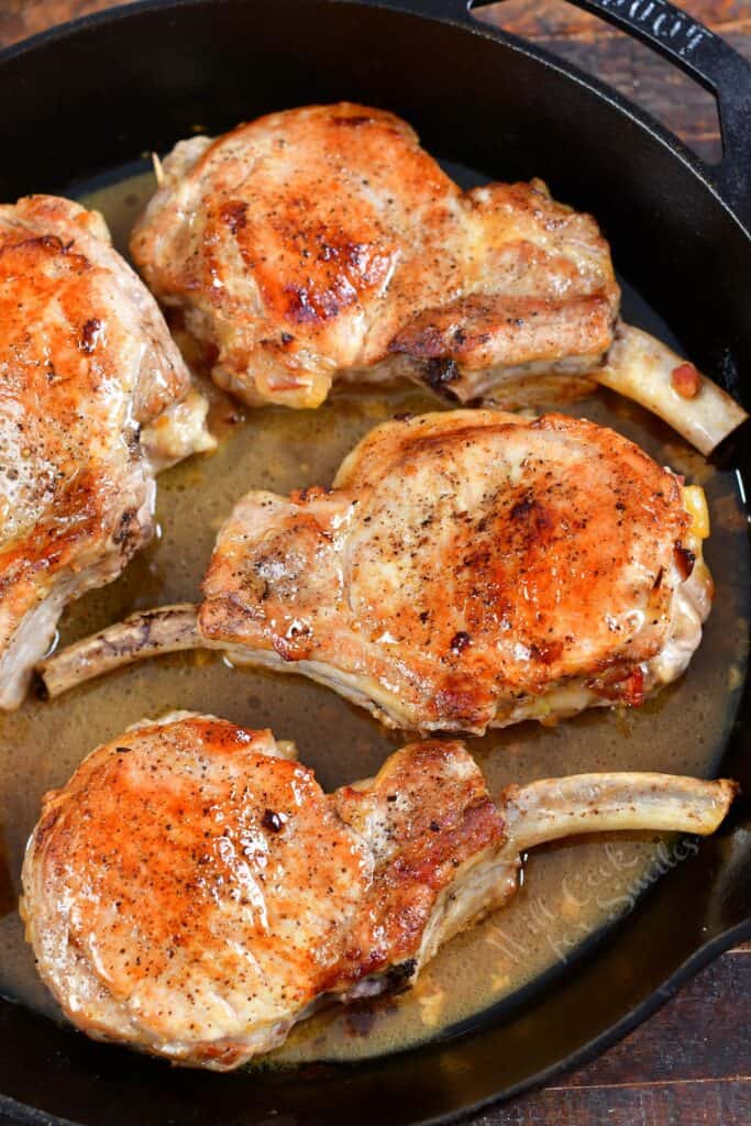 Four pork chops are cooked in a skillet.